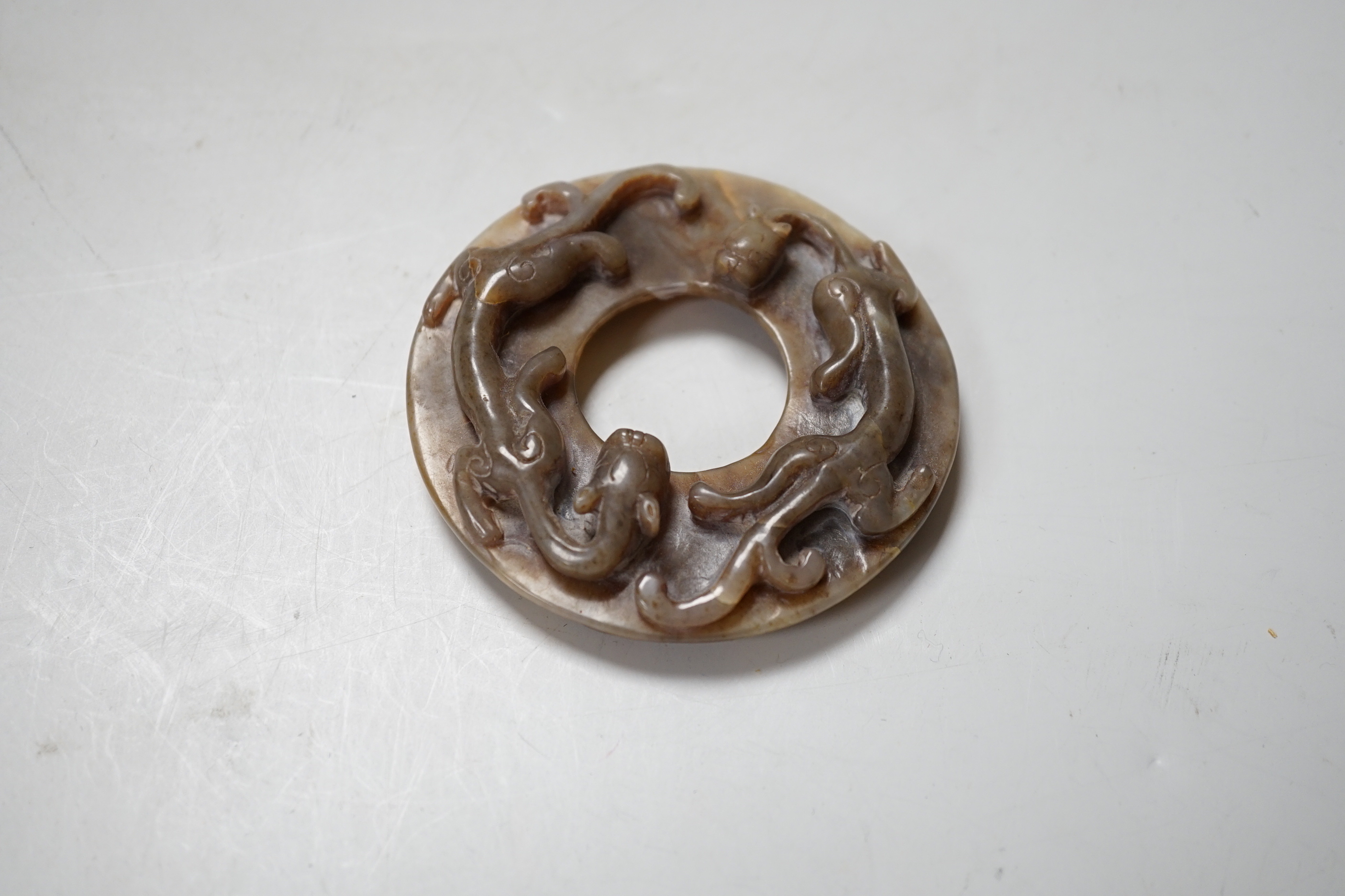 A Chinese brown and celadon jade ‘chilong’ bi disc, probably Ming dynasty, 8cm